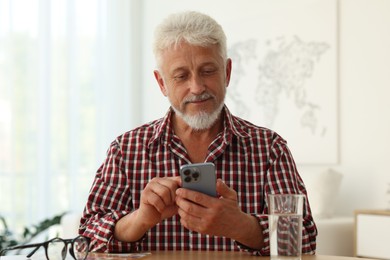 Senior man using smartphone at table indoors