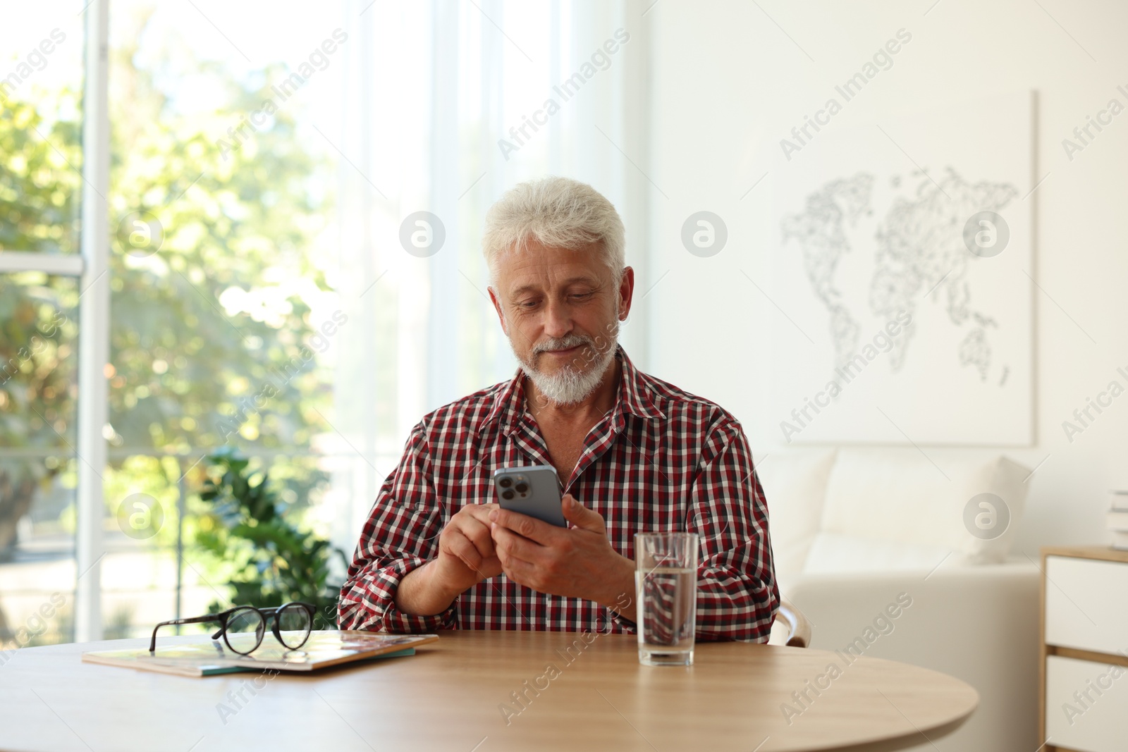 Photo of Senior man using smartphone at table indoors