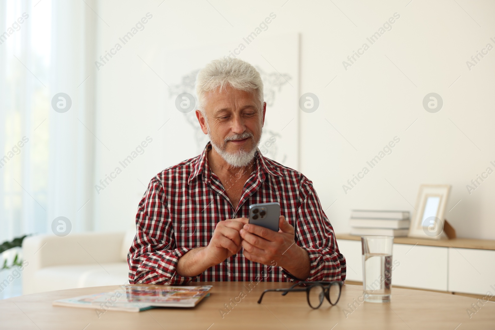 Photo of Senior man using smartphone at table indoors