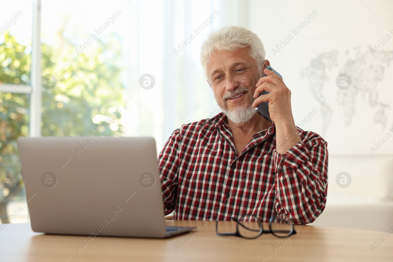 Photo of Senior man talking on phone at table indoors