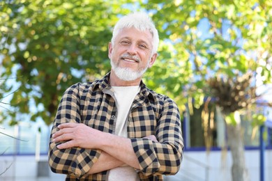 Photo of Portrait of smiling senior man with crossed arms outdoors