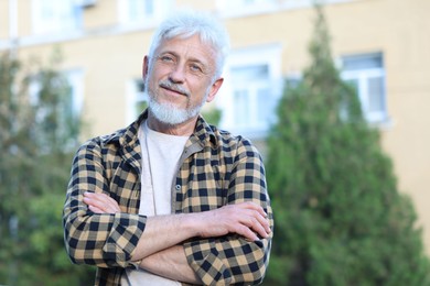 Photo of Portrait of senior man with crossed arms outdoors, space for text