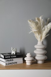 Photo of Different decorative elements and books on chest of drawers near gray wall indoors