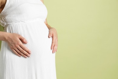 Photo of Young pregnant woman on light olive background, closeup. Space for text