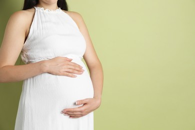 Photo of Young pregnant woman on light olive background, closeup. Space for text