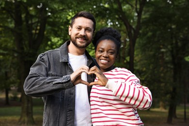 International relationships. Lovely couple making heart with hands outdoors