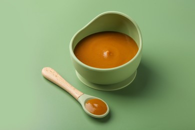 Photo of Delicious baby food in bowl with spoon on green table