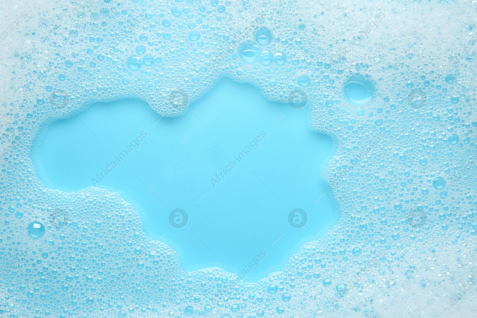 Photo of Washing laundry. White foam with bubbles on light blue background, top view