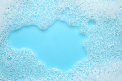 Photo of Washing laundry. White foam with bubbles on light blue background, top view