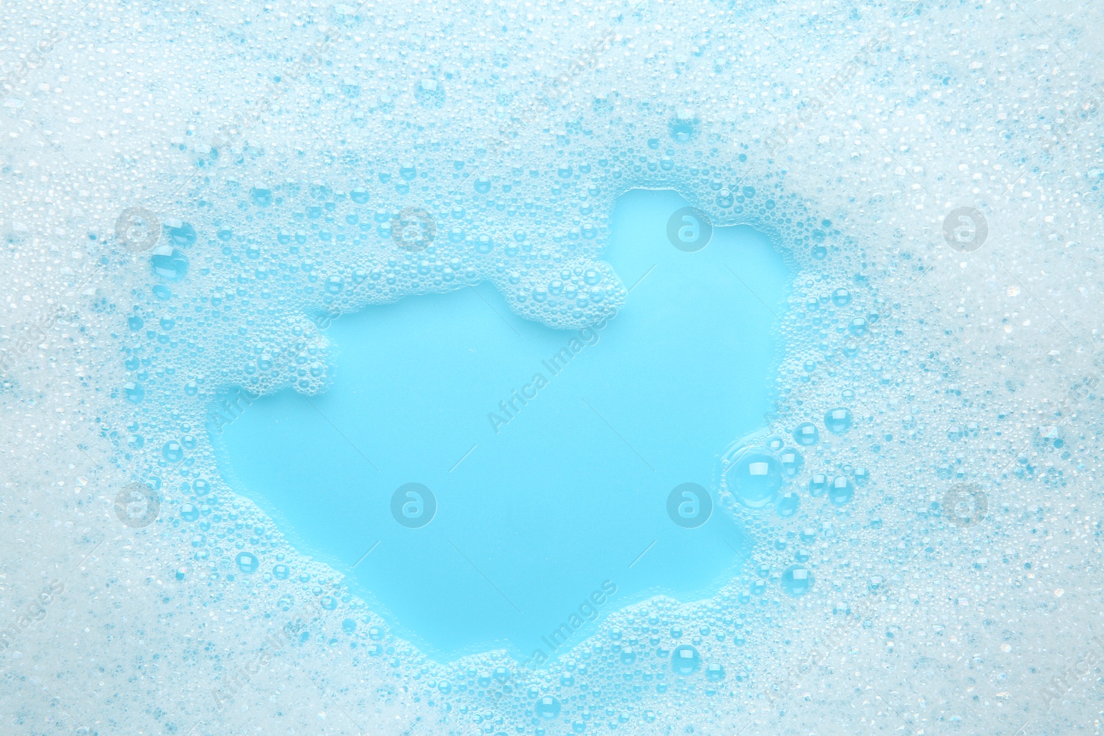 Photo of Washing laundry. White foam with bubbles on light blue background, top view