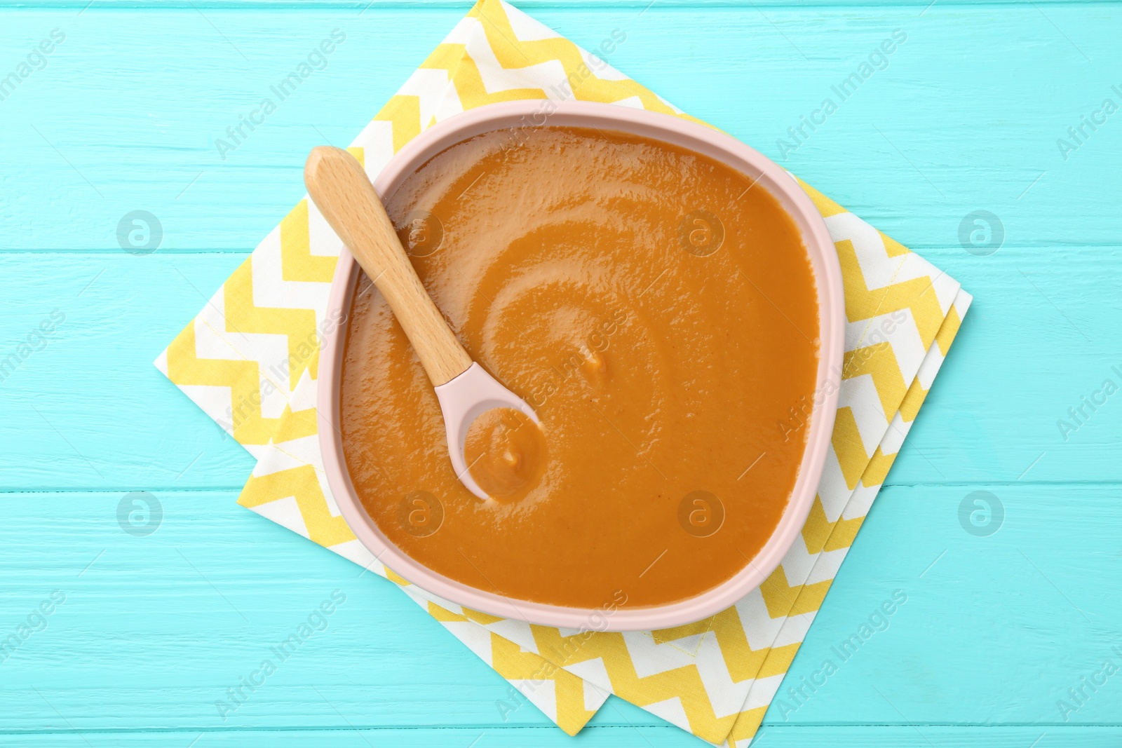 Photo of Delicious baby food in bowl on light blue wooden table, top view