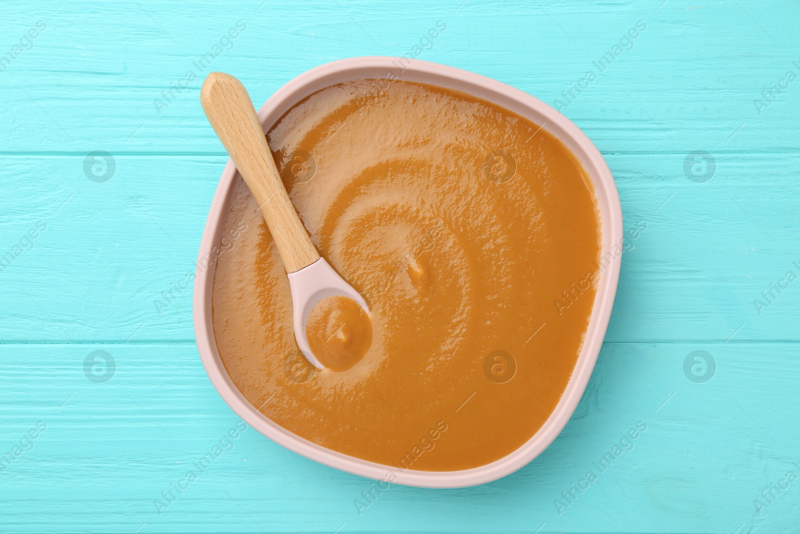 Photo of Delicious baby food in bowl on light blue wooden table, top view