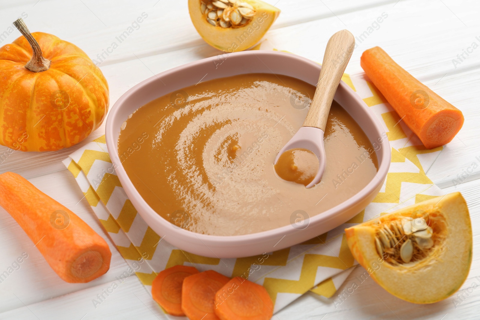 Photo of Delicious baby food in bowl and ingredients on white wooden table, closeup