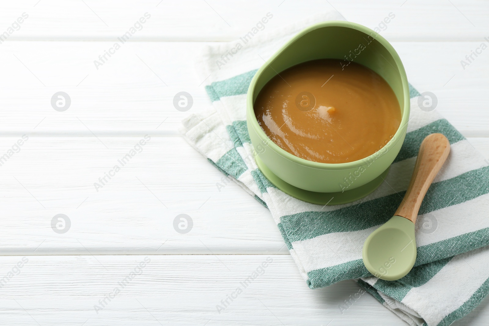 Photo of Delicious baby food in bowl on white wooden table. Space for text