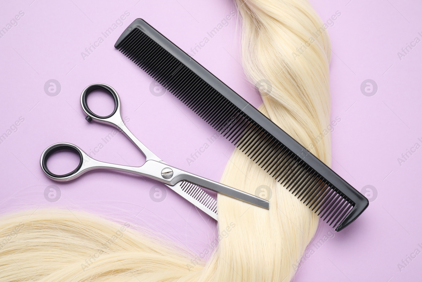 Photo of Blonde hair strand, comb and professional scissors on violet background, top view