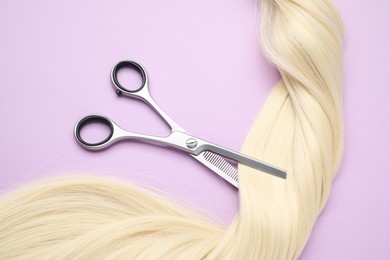 Photo of Blonde hair strand and professional scissors on violet background, top view