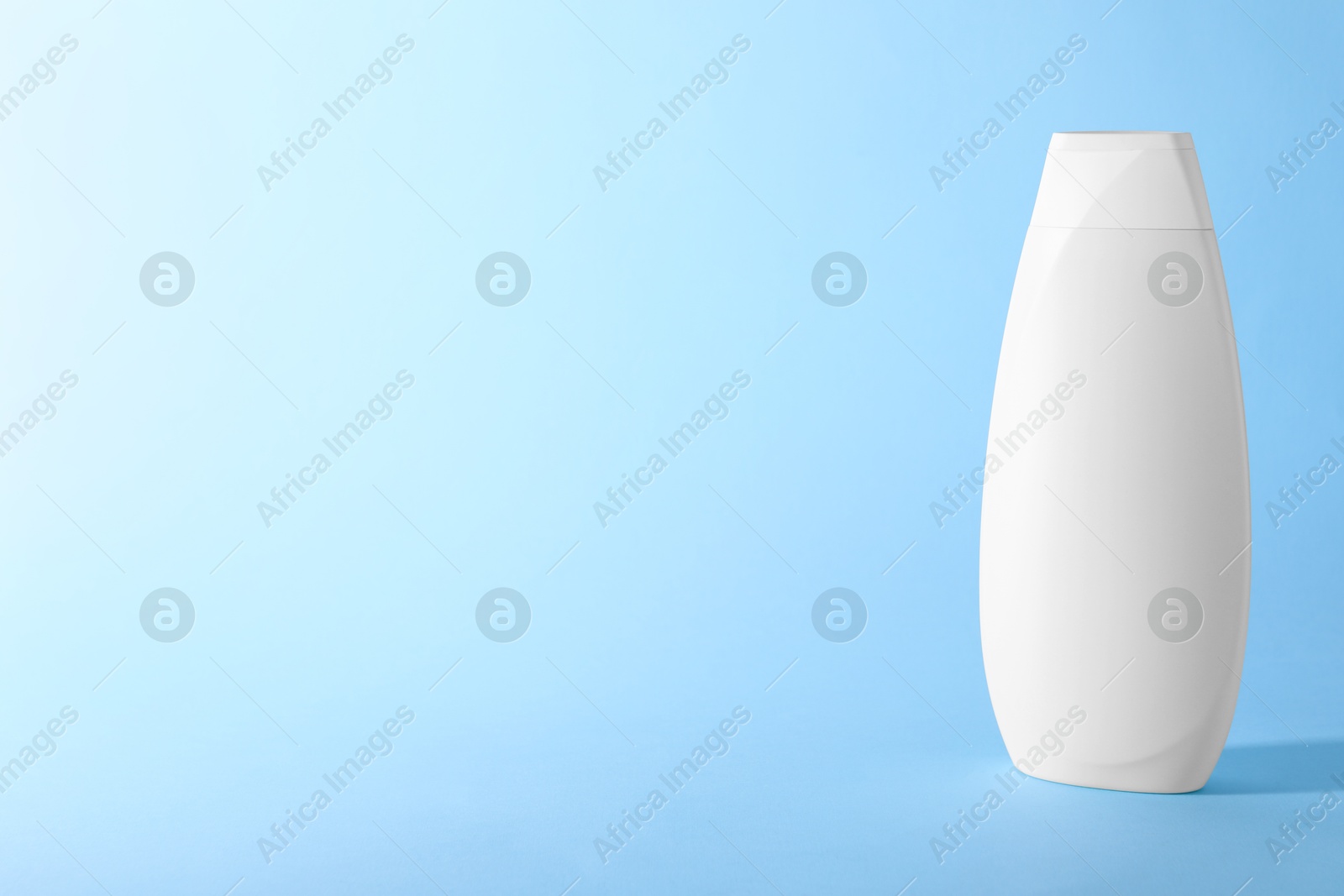 Photo of Shampoo in container on light blue background, space for text