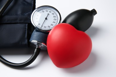 Photo of Blood pressure measuring device and red decorative heart on light background, closeup