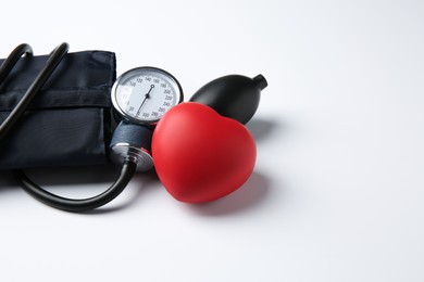 Photo of Blood pressure measuring device and red decorative heart on light background, space for text