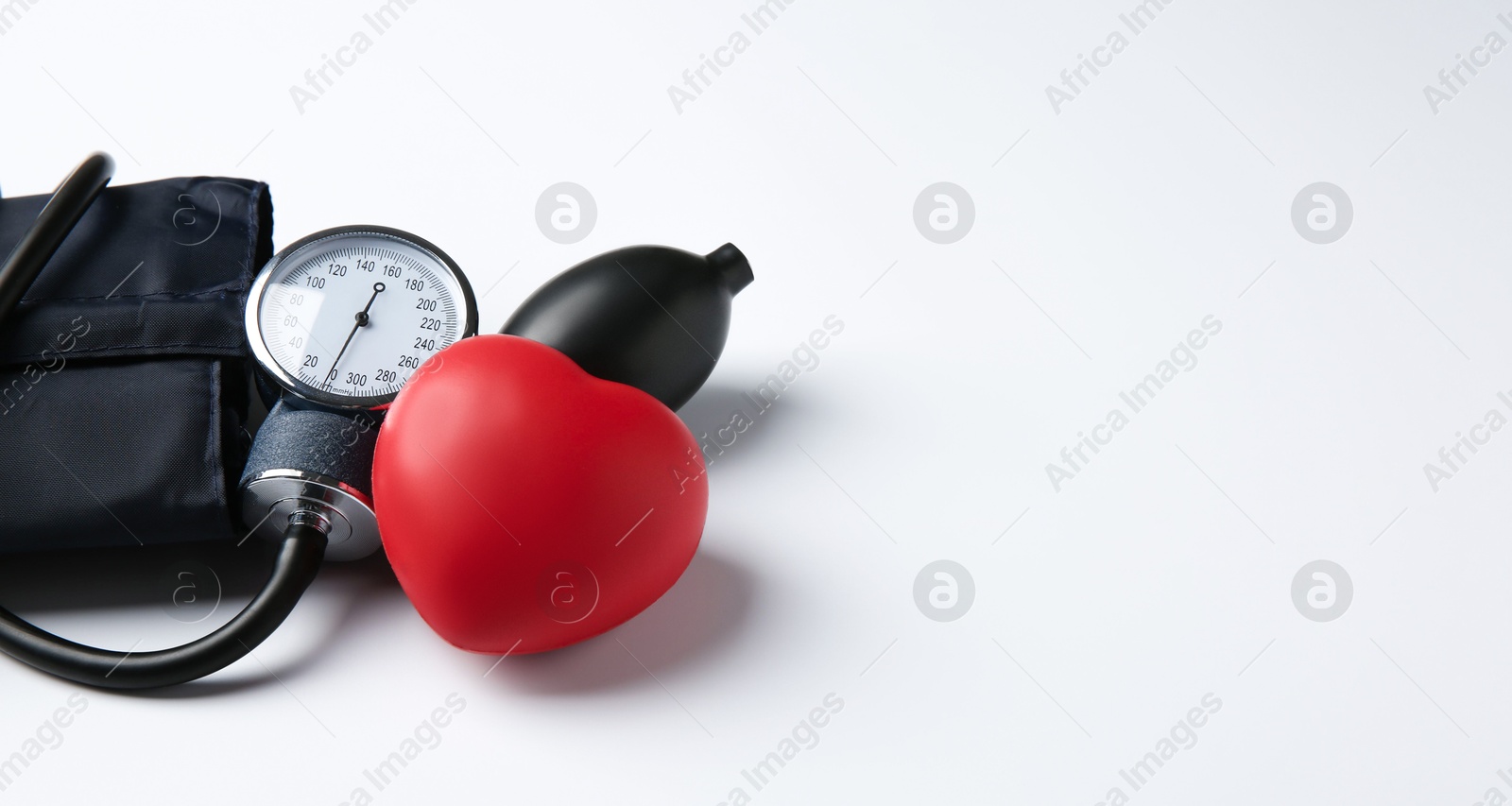 Photo of Blood pressure measuring device and red decorative heart on light background, space for text