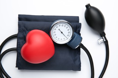 Photo of Blood pressure measuring device and red decorative heart on light background, top view