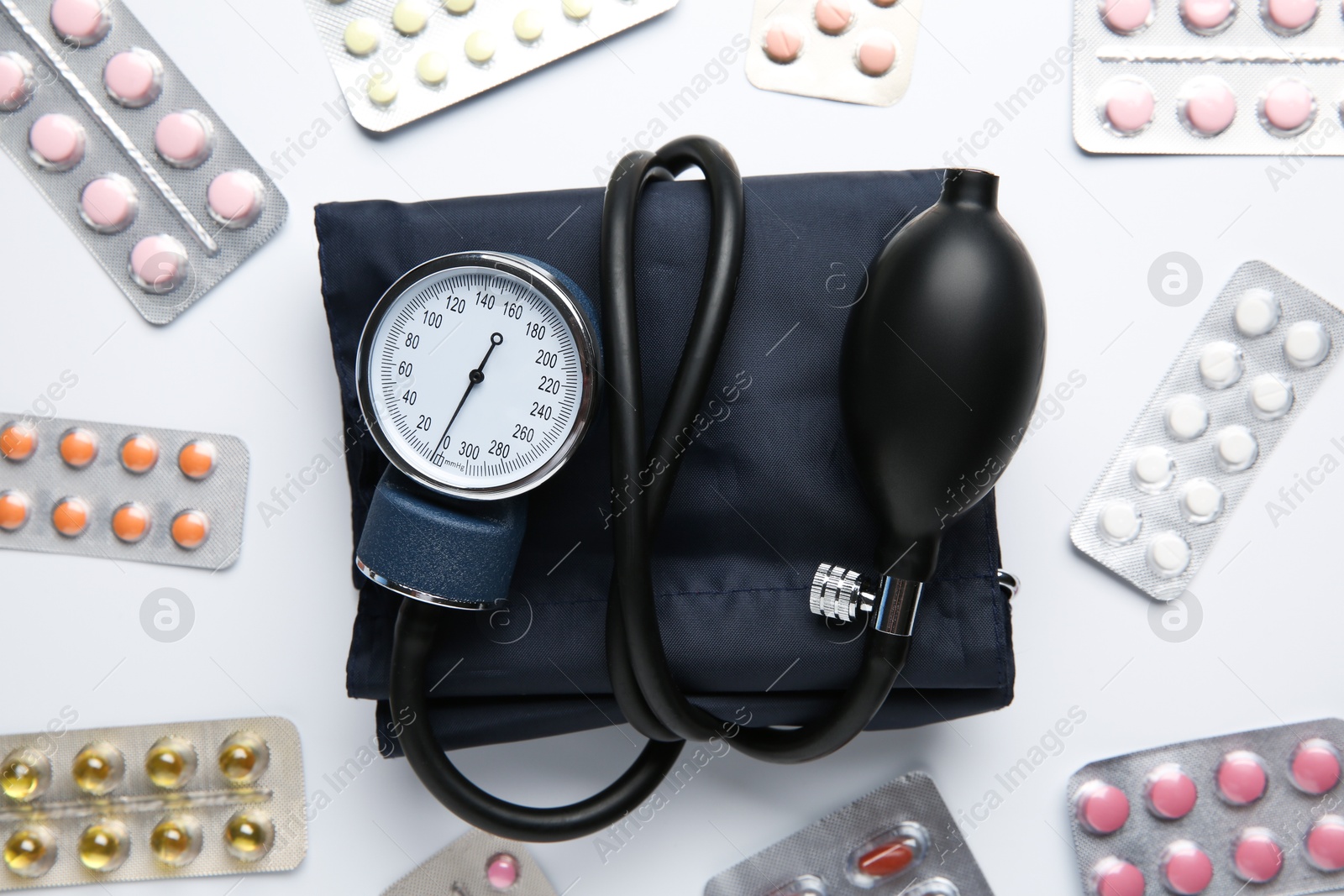 Photo of Blood pressure measuring device and pills in blisters on light background, flat lay