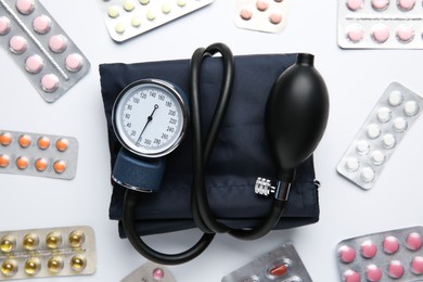 Blood pressure measuring device and pills in blisters on light background, flat lay