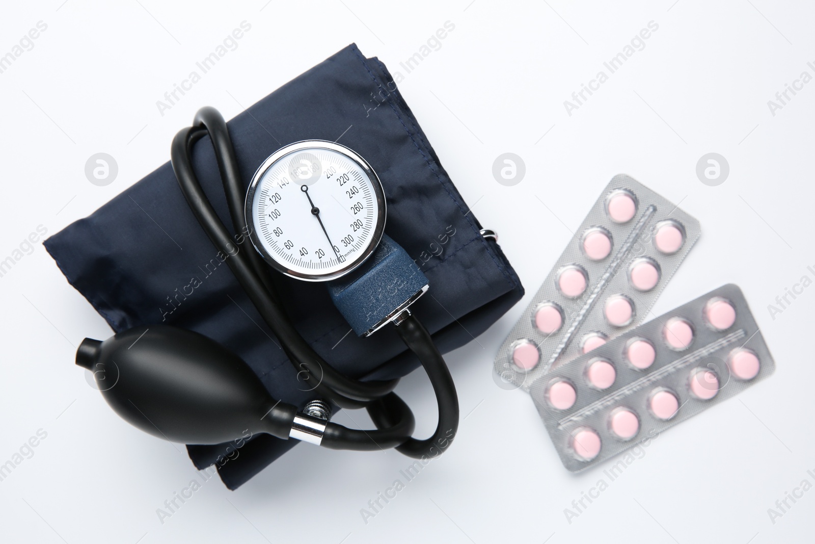 Photo of Blood pressure measuring device and pills in blisters on light background, flat lay