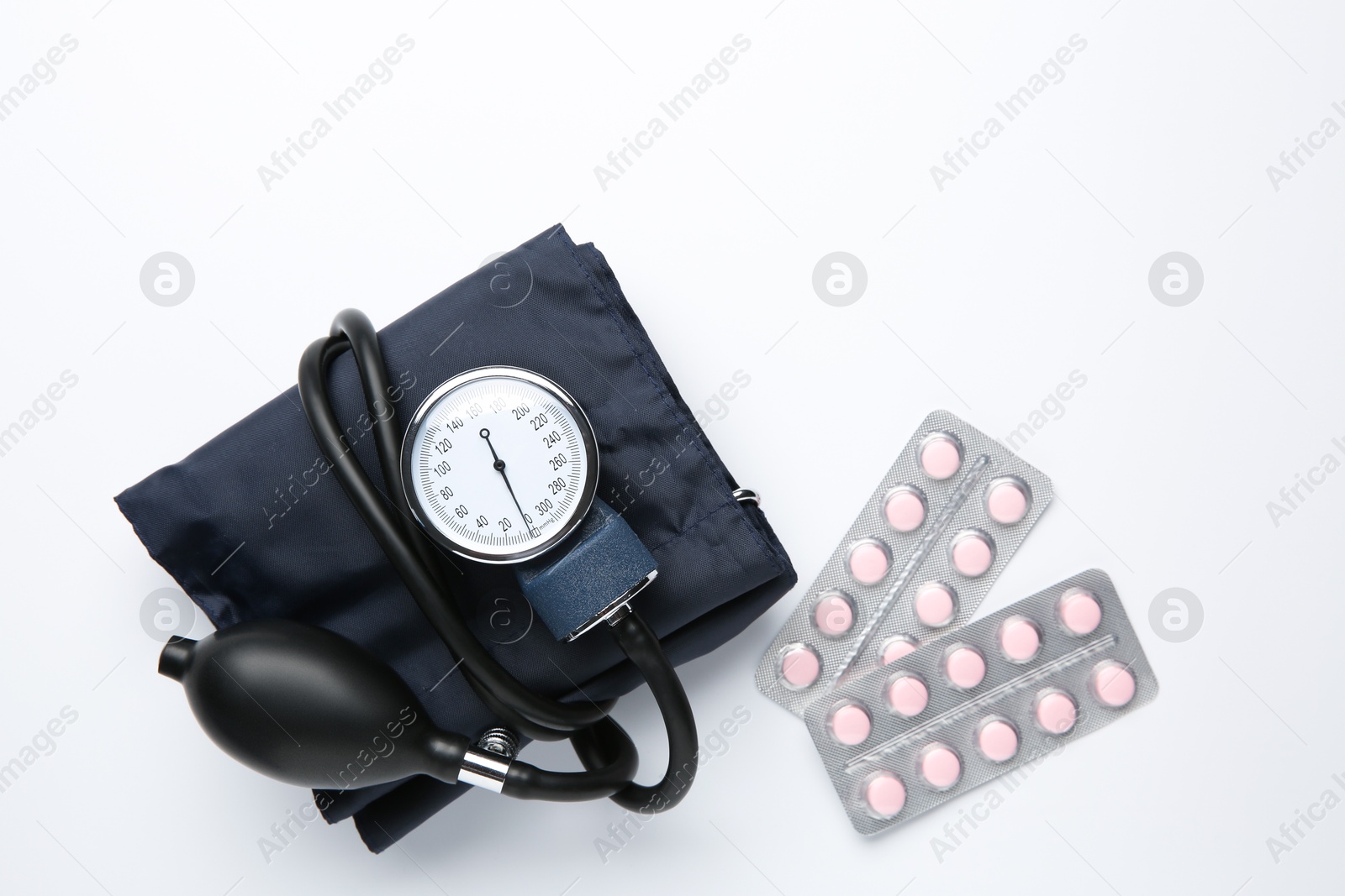 Photo of Blood pressure measuring device and pills in blisters on light background, flat lay