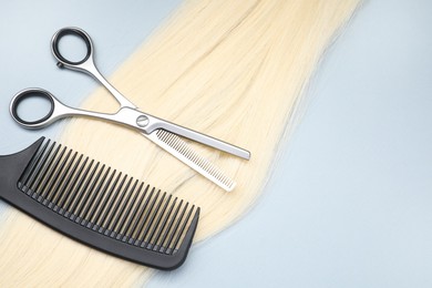 Photo of Blonde hair strand, comb and professional scissors on light grey background, top view