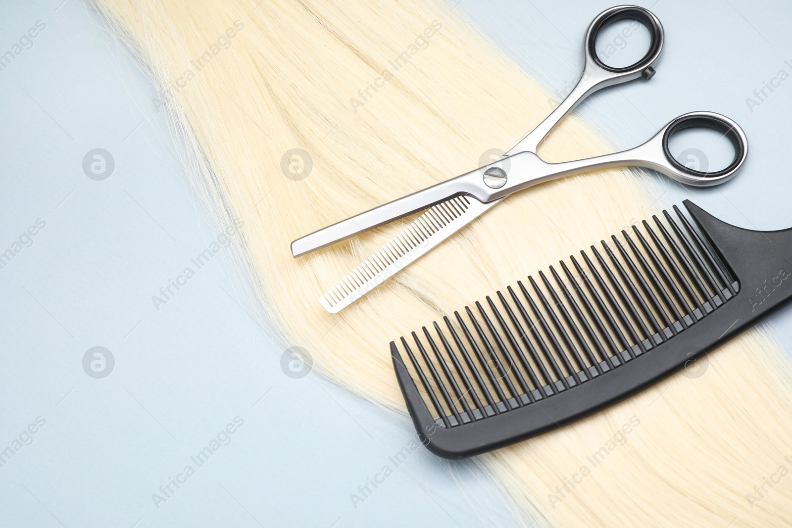 Photo of Blonde hair strand, comb and professional scissors on light grey background, top view