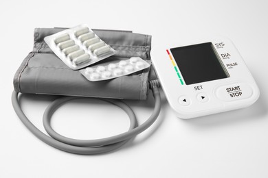 Photo of Blood pressure measuring device and pills on white background, closeup