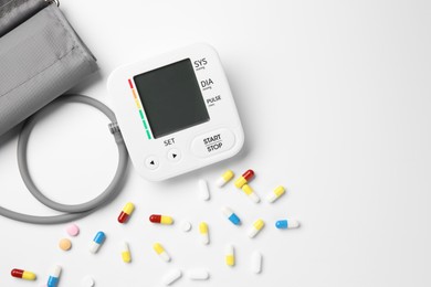 Photo of Blood pressure measuring device and pills on white background, top view. Space for text