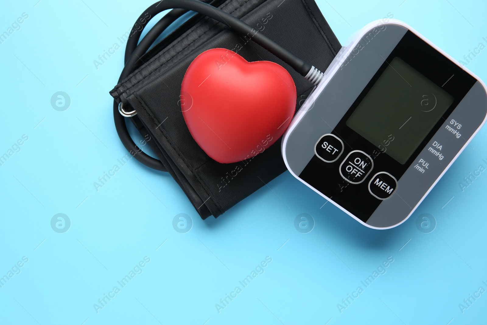 Photo of Blood pressure measuring device and squeeze heart on light blue background, top view