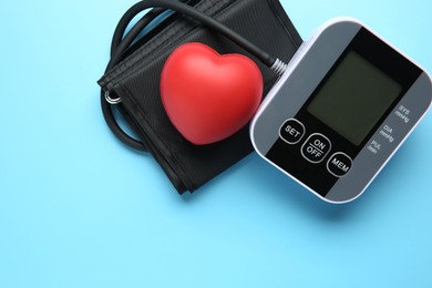 Blood pressure measuring device and squeeze heart on light blue background, top view