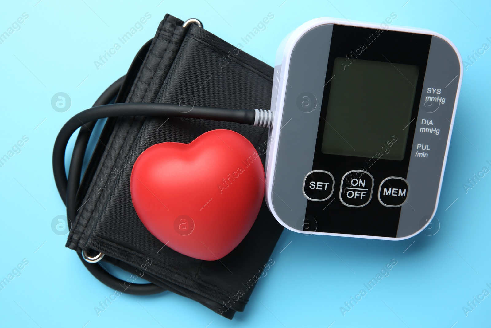 Photo of Blood pressure measuring device and squeeze heart on light blue background, top view