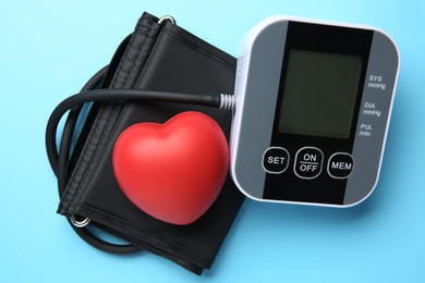 Photo of Blood pressure measuring device and squeeze heart on light blue background, top view