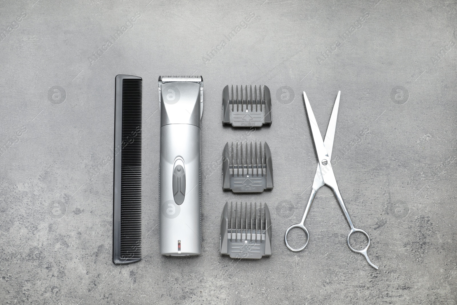 Photo of Professional hair clipper with guards, comb and scissors on grey surface, flat lay