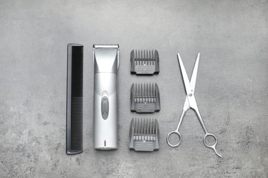 Photo of Professional hair clipper with guards, comb and scissors on grey surface, flat lay