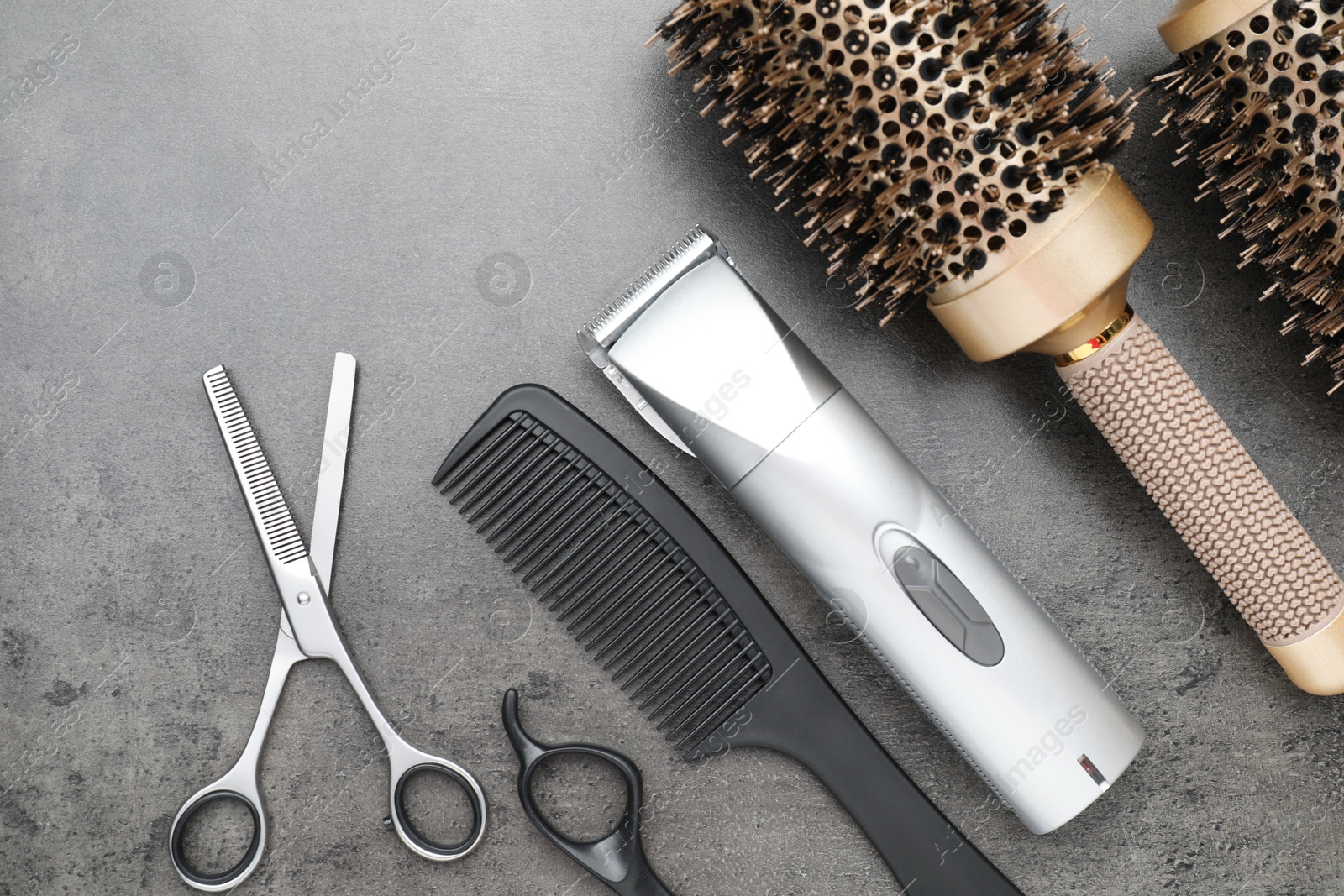 Photo of Professional hair clipper, different combs and scissors on grey surface, flat lay