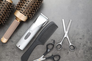 Photo of Professional hair clipper, different combs and scissors on grey surface, flat lay