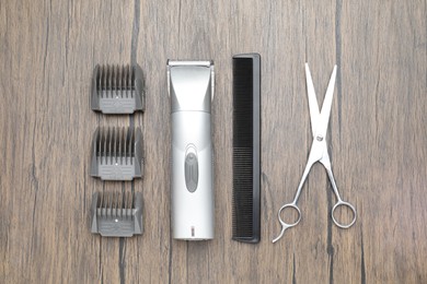 Photo of Professional hair clipper with guards, comb and scissors on wooden surface, flat lay