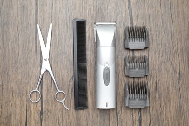 Photo of Professional hair clipper with guards, comb and scissors on wooden surface, flat lay