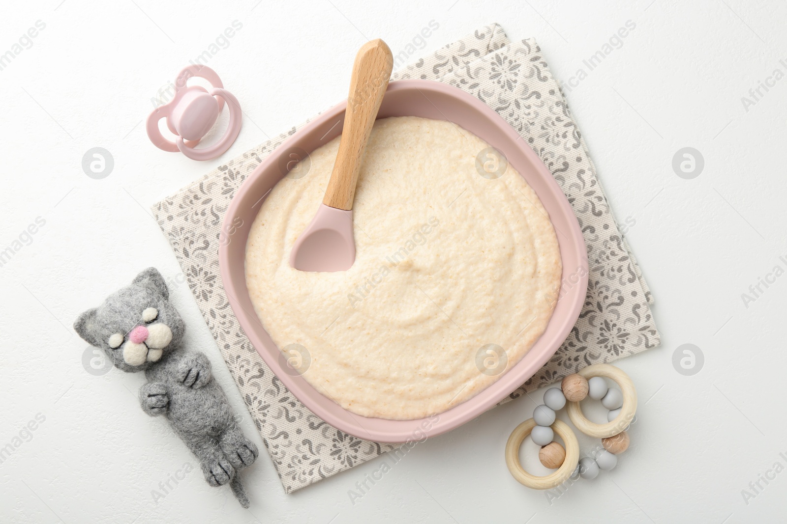 Photo of Delicious baby food in bowl with spoon, pacifier and toys on white background, flat lay