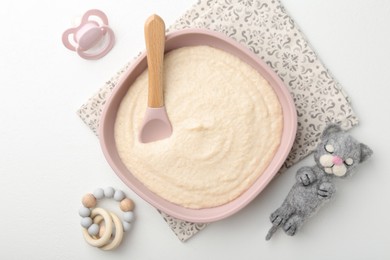 Photo of Delicious baby food in bowl with spoon, pacifier and toys on white background, flat lay