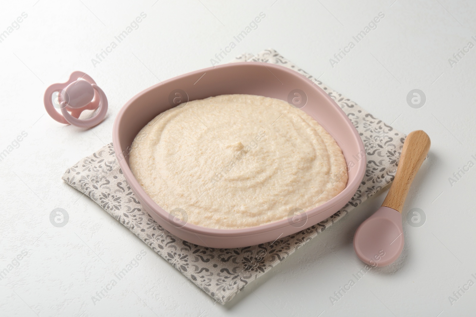 Photo of Delicious baby food in bowl with spoon and pacifier on white background