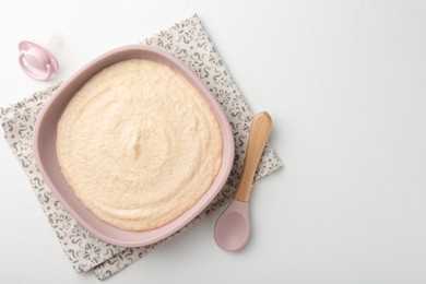 Photo of Delicious baby food in bowl with spoon and pacifier on white background, top view. Space for text