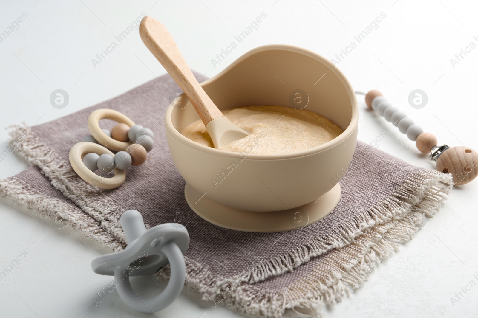 Photo of Delicious baby food in bowl with spoon, pacifier and teether on white background