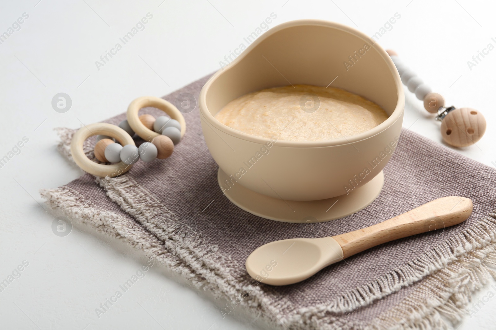 Photo of Delicious baby food in bowl with spoon and teether on white background