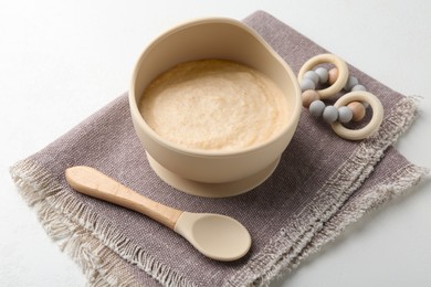 Photo of Delicious baby food in bowl with spoon and teether on white background